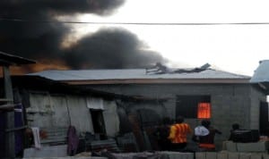 Some houses gutted by fire at Sari Iganmu in Lagos last Wednesday, on the roof as a man removing roofing sheets from a near by house during the fire incident recently.